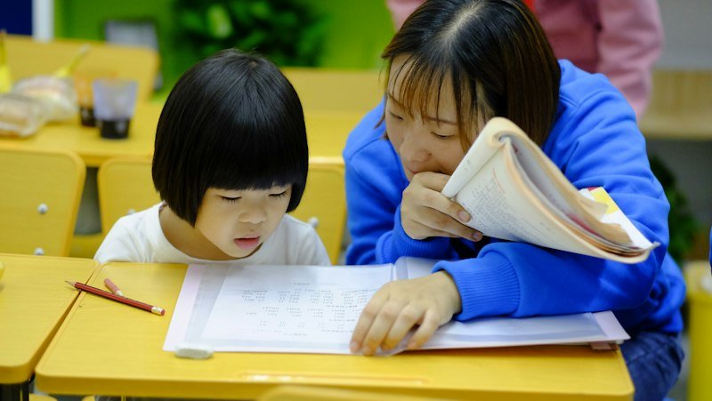 A tutor guiding a pupil through her work at a desk