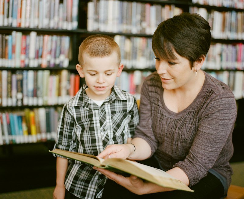 A tutor reading with a young pupil in a library